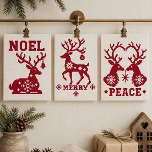 May include: Three rectangular white fabric panels featuring red cross-stitch embroidery. The left panel displays a reindeer and the word NOEL. The center panel shows a reindeer and the word MERRY. The right panel depicts two reindeer and the word PEACE.