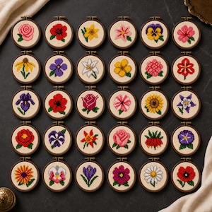 May include: A collection of thirty circular wooden embroidery hoops, each containing a unique cross-stitch pattern of a different flower. The flowers are rendered in vibrant colours including red, yellow, pink, purple, and white, set against a light fabric.