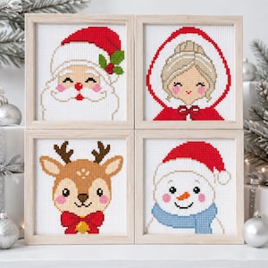 May include: Four square cross-stitch artworks in light wood frames. The top left shows Santa Claus, the top right shows a person in a red hood, the bottom left shows a reindeer with a red bow, and the bottom right shows a snowman with a blue scarf.