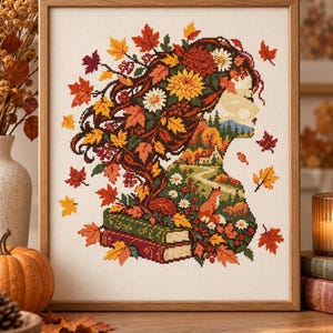 May include: A cross-stitch embroidery in a wooden frame depicting a side profile silhouette of a person. The hair is composed of autumn leaves and flowers, while the body contains a landscape with a house, a path, a fox, and two stacked books.