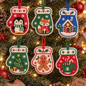 Könnte beinhalten: Ein Set aus sechs im Kreuzstich gearbeiteten Fäustling-Anhängern mit weihnachtlichen Motiven wie einem Pinguin, einem Fuchs, einem Lebkuchenhaus, einem Weihnachtsbaum, einem Lebkuchenmann und einer Tasse mit heißer Schokolade.