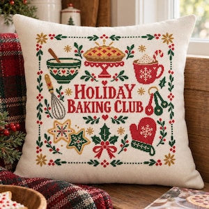 May include: A square off-white throw pillow featuring a cross-stitch design with the text "Holiday Baking Club" in red. The pattern includes a pie, a mug with a candy cane, a whisk, measuring spoons, a star cookie, and a red oven mitt.