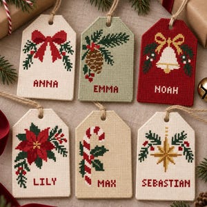 May include: Six rectangular cross-stitch gift tags with jute twine loops. Designs include a red bow, pinecone, bell, poinsettia, candy cane, and star. Each tag features a name: Anna, Emma, Noah, Lily, Max, or Sebastian, stitched in red letters.