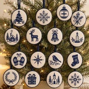 May include: A collection of sixteen circular ornaments featuring navy blue cross-stitch designs on cream fabric. Each ornament has a dark blue ribbon loop for hanging and displays unique holiday motifs including trees, snowflakes, a deer, and a bell.
