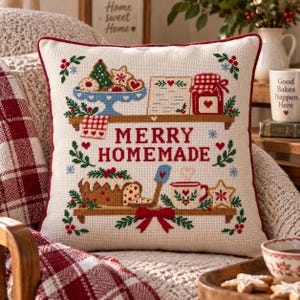 Puede incluir: Un cojín cuadrado con base de tela color crema y ribete rojo. La parte frontal presenta un diseño de punto de cruz de dos estantes de madera con productos horneados, un tarro y una taza, con el texto rojo MERRY HOMEMADE en el centro.