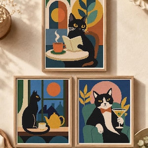 May include: Three framed cross-stitch art pieces featuring cats. The top piece shows a black cat reading at a table with a coffee cup. The bottom left shows a black cat by a window with a teapot. The bottom right shows a tuxedo cat holding a martini.