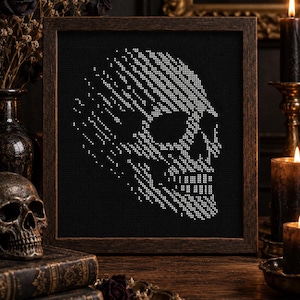 May include: A square wooden frame containing a cross-stitch embroidery on black fabric. The embroidery features a white skull design created with individual stitches, showing a side profile of a human skull with a pixelated or fragmented effect.