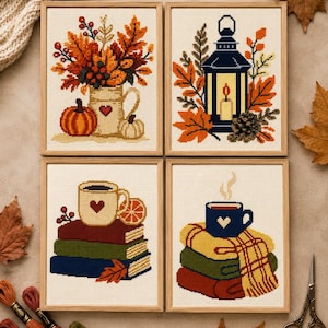 May include: Four framed cross-stitch patterns featuring autumn themes: a pitcher with leaves and pumpkins, a lantern with foliage, a mug on a stack of books with an orange slice, and a mug on a stack of folded blankets, all in light wood frames.