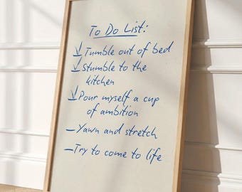 May include: A rectangular framed print with a light wood frame featuring the text To Do List: Tumble out of bed, Stumble to the kitchen, Pour myself a cup of ambition, Yawn and stretch, and Try to come to life written in blue ink.