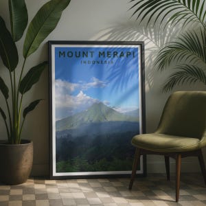 Puede incluir: Una impresión de arte mural rectangular enmarcada que presenta una fotografía de paisaje del Monte Merapi en Indonesia. La imagen muestra un pico de montaña verde bajo un cielo azul con nubes blancas, con el texto MOUNT MERAPI INDONESIA arriba.