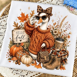 Könnte beinhalten: Ein weißes T-Shirt mit einer Grafik einer Gans, die einen orangefarbenen Zopfmuster-Pullover, eine Leoparden-Schleife und eine Sonnenbrille trägt. Die Gans hält eine Leoparden-Handtasche. Dazu gehören Kürbisse, Herbstblätter, ein Schild mit der Aufschrift Hello fall und ein Becher mit der Aufschrift Pumpkin Spice Season.