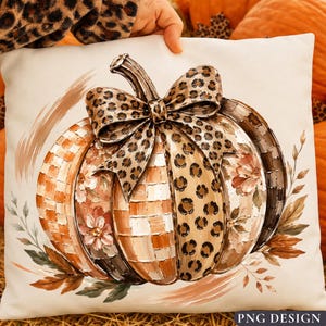 Puede incluir: Un cojín cuadrado con una ilustración central de una calabaza con un lazo de estampado de leopardo. La calabaza tiene segmentos alternos de cuadros naranjas, estampado de leopardo y motivos florales. Hojas marrones rodean la base.