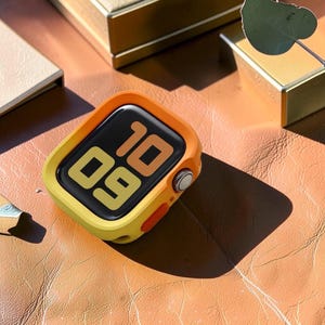Pode incluir: Um smartwatch com uma capa protetora amarela brilhante e laranja. O visor digital mostra a hora 10:09 com uma fonte clara e ousada. O relógio possui uma coroa lateral prateada e um botão laranja proeminente na lateral da caixa.