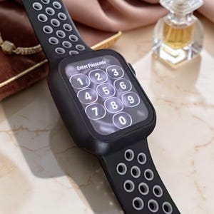 Könnte beinhalten: Eine schwarze Smartwatch mit rechteckigem Display, das ein Tastenfeld und den Text Enter Passcode anzeigt. Die Uhr hat ein flexibles Silikonarmband mit kreisförmigen Ausstanzungen, die eine hellgraue Innenschicht zum Vorschein bringen.