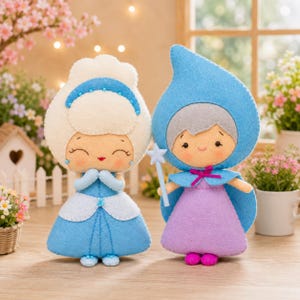 Pode incluir: Duas bonecas de feltro. A boneca da esquerda tem cabelo branco, uma faixa azul e um vestido azul. A boneca da direita usa uma capa azul com capuz sobre um vestido roxo e segura uma varinha de estrela azul clara. Rostos bordados.