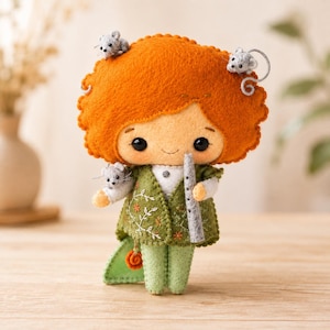 May include: A felt doll with bright orange hair, wearing a green vest with white floral embroidery and light green pants. The doll holds a grey flute and has three small grey mice attached to its hair and hand, featuring black bead eyes.