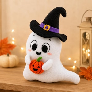 May include: A white felt ghost figurine wearing a black witch hat with a purple band and yellow buckle. The ghost has large black eyes, a small smile, and pink cheeks, and is holding a small orange felt pumpkin with a carved jack-o'-lantern face.