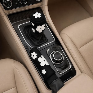 Può includere: Un copri pomello del cambio nero e una copertura per la leva del freno a mano nera abbinata, entrambi caratterizzati da un motivo floreale bianco ripetuto. Questi accessori per interni auto sono progettati per coprire il cambio e il freno.