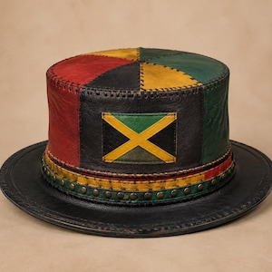 May include: A leather top hat featuring a patchwork design in red, yellow, green, and black. The crown displays a rectangular patch of the Jamaican flag. The base of the crown is accented with a yellow leather band and a row of metallic studs.