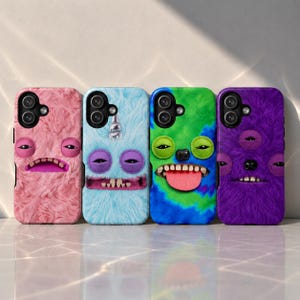 May include: Four smartphone cases with fuzzy, textured surfaces in pink, light blue, green and blue tie-dye, and purple. Each case features a unique monster face with protruding eyes, teeth, and tongues, along with cutouts for camera lenses.