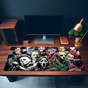 May include: A rectangular desk mat featuring a colourful graphic illustration of various horror movie characters, including a masked figure with a knife, a hockey mask, a clown, and a hooded ghost face, arranged in a dense collage pattern.