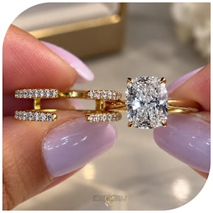May include: A gold ring set consisting of a solitaire ring with a large cushion-cut clear stone and a separate open-style band featuring two rows of small clear pavé stones. The rings are crafted from a polished yellow gold-toned metal.