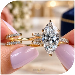 May include: A gold ring featuring a large marquise-cut clear gemstone held by six prongs. The band is split into two distinct rows, both encrusted with small, round, clear pavé stones that extend along the sides of the central marquise setting.