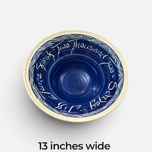 May include: A round ceramic bowl measuring 33 cm wide with a deep blue interior featuring concentric rings. The rim has a white wavy pattern on a blue background with the white handwritten text: First Two Thousand two - Shirley - Jiss - June.
