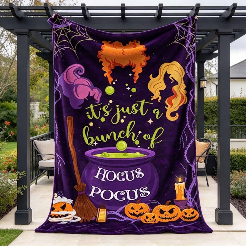 May include: A purple fleece blanket featuring a graphic print of three distinct hairstyles, a broomstick, a bubbling cauldron, and jack-o'-lanterns. The text reads, "it's just a bunch of HOCUS POCUS" in yellow and white lettering against a dark background.