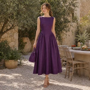 Puede incluir: Un vestido midi sin mangas de color morado intenso con un corpiño ajustado y una falda amplia plisada. El vestido presenta un cuello redondo y un pequeño bolso morado a juego que se sostiene en la mano. La tela tiene un acabado tipo lino.