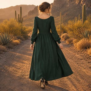 Puede incluir: Un vestido largo de color verde oscuro con mangas largas, un corpi&ntilde;o ajustado y una falda amplia y fluida. La prenda presenta un escote ancho y redondeado que deja al descubierto la parte superior de la espalda y los hombros, con pu&ntilde;os.