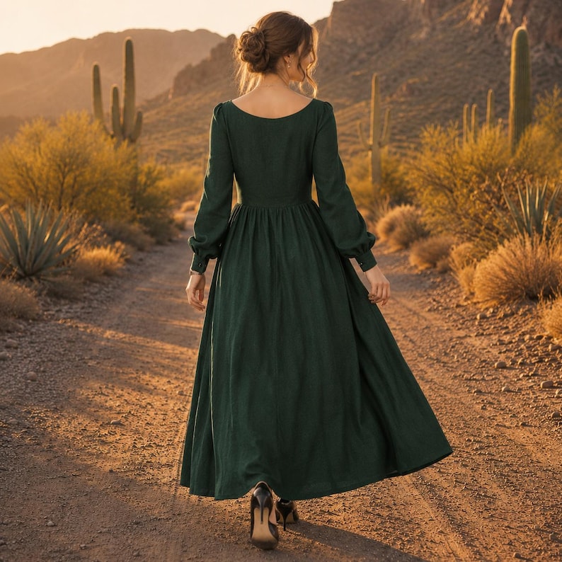Puede incluir: Un vestido largo de color verde oscuro con mangas largas, un corpi&ntilde;o ajustado y una falda amplia y fluida. La prenda presenta un escote ancho y redondeado que deja al descubierto la parte superior de la espalda y los hombros, con pu&ntilde;os.