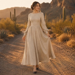 Puede incluir: Un vestido beige de manga larga que llega hasta el suelo, con un corpi&ntilde;o ajustado, cuello redondo y una falda amplia y fluida. El vestido presenta mangas con pu&ntilde;os y un dise&ntilde;o de tela de color s&oacute;lido que llega hasta los tobillos.