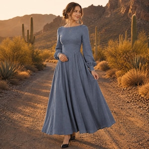 Puede incluir: Un vestido largo hasta el suelo de color azul polvoriento con mangas largas. La prenda presenta un corpi&ntilde;o ajustado, un escote redondeado y una falda amplia y fluida que llega hasta el suelo. Las mangas son largas y tienen pu&ntilde;os fruncidos.