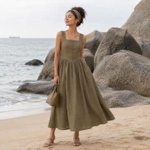 Puede incluir: Un vestido midi de color verde oliva con escote cuadrado, un corpiño ajustado con una hilera vertical de botones a juego y una falda amplia y fruncida. El vestido se combina con una diadema verde oliva a juego y un pequeño bolso de mano.