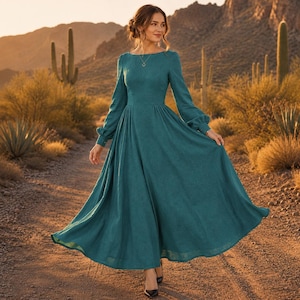 Puede incluir: Un vestido largo hasta los pies, de color azul verdoso profundo, con mangas largas. La prenda presenta un corpi&ntilde;o ajustado, un escote redondeado y una falda amplia y fluida que llega hasta los tobillos. La tela tiene una textura sutil.