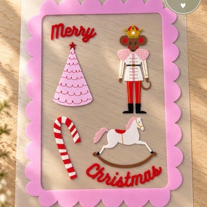 Könnte beinhalten: Ein rechteckiges A5-Blatt mit einem gewellten rosa Rand und dem roten Schriftzug Merry Christmas. Das Design zeigt einen rosa Weihnachtsbaum, eine Maus als Soldat mit Krone, eine rot-weiße Zuckerstange und ein weißes Schaukelpferd.