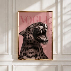 May include: A framed wall art print featuring a black and white leopard with its mouth open in a roar, set against a solid dusty pink background. The word VOGUE is printed in large, bold, capital letters across the top of the leopard image.