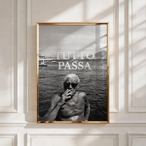 May include: A black and white framed wall art print featuring a shirtless person wearing sunglasses, smoking, and standing by the sea. The text TUTTO PASSA is printed in white over the water and also appears as a tattoo on the person's chest.