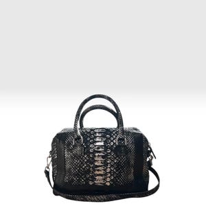 May include: A black and silver handbag featuring a textured snakeskin pattern across the front and sides. The bag includes two top handles, silver-toned metal hardware, and a detachable shoulder strap attached to the sides with metal clips.
