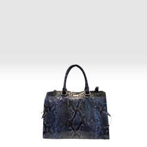 Puede incluir: Un bolso estructurado con un patrón de piel de serpiente en azul y negro. El bolso tiene dos asas superiores, una base rectangular y herrajes metálicos que conectan las asas con el cuerpo principal. La textura imita escamas de reptil.