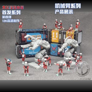 May include: A collection of miniature figurines featuring two grey robotic arms and several small figures in red and white uniforms. The figures are positioned around and on top of stacked, rectangular storage containers with blue and yellow panels.