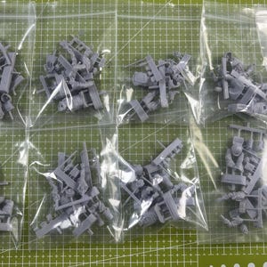 May include: Eight clear plastic bags containing unpainted grey resin miniature soldier figures on sprues. Each bag holds multiple small, detailed components for assembly, including torsos, limbs, and equipment, all cast in a uniform matte grey resin material.