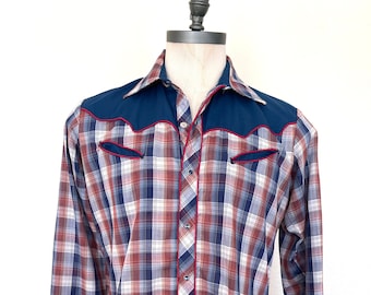 May include: A long-sleeved plaid shirt with a blue and red plaid pattern. The shirt has a dark blue yoke with red stitching and two chest pockets with red stitching.
