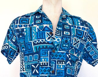 Op de afbeelding: Een blauw en wit overhemd met korte mouwen en knopen met een geometrisch patroon. Het patroon bevat verschillende vormen en ontwerpen, waaronder vierkanten, driehoeken en cirkels.