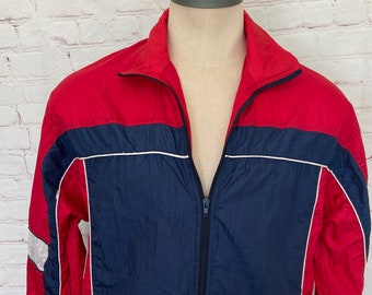 May include: A red and navy blue windbreaker jacket with white piping. The jacket has a zipper closure and long sleeves.