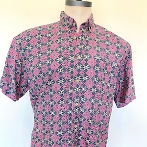 May include: A short-sleeved button-down shirt with a geometric pattern in shades of pink, black, and cream.
