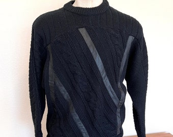 May include: Black cable knit sweater with black leather panels. The sweater has a crew neck and long sleeves.