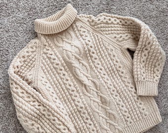 May include: A cream-colored cable knit sweater with a turtleneck.
