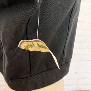 May include: Black denim jacket with a small tag attached to the bottom. The tag is cream colored with green leaves and blue stripes.